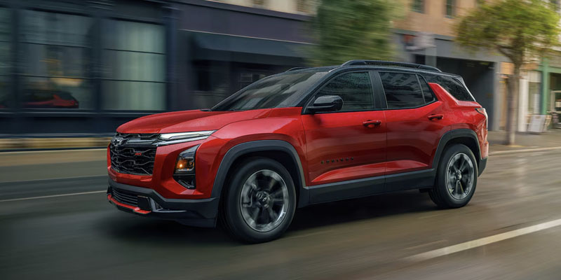 A vibrant red 2025 Chevrolet Equinox cruising down a bustling downtown street near Roscommon, MI, on a sunny day, with lush green trees and detailed city buildings in the background.