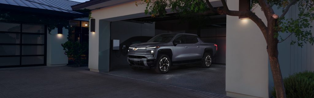 A silver 2025 Chevy Silverado EV parked in the garage of a modern home near Seminole Chevrolet in Seminole, OK, highlighting its sleek design and electric innovation.
