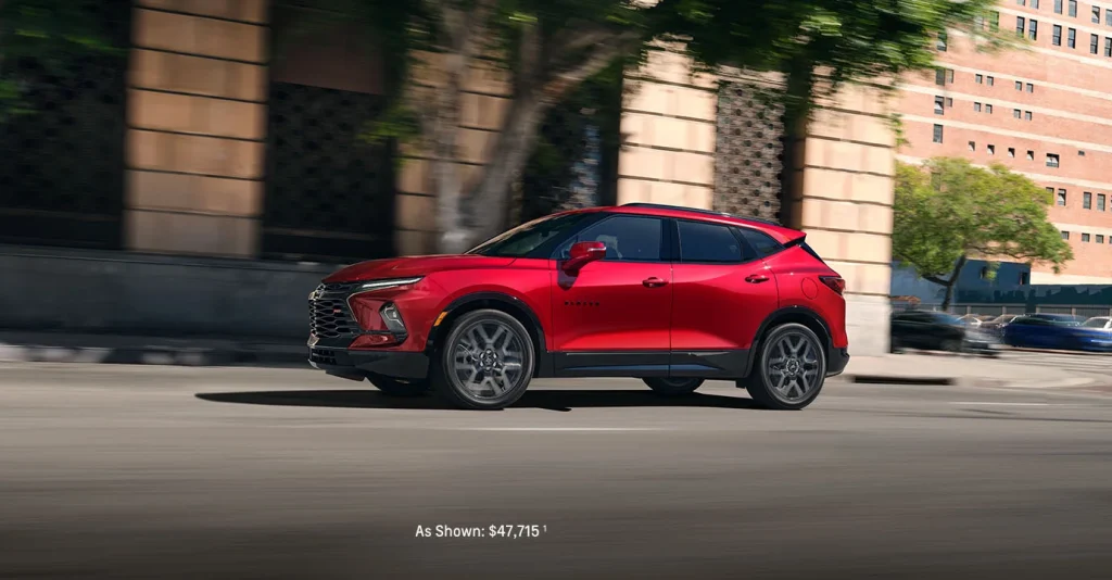 A red 2025 Chevy Blazer driving through a downtown city street near Don Nester Chevrolet in Roscommon, Michigan, showcasing its bold styling and urban versatility.