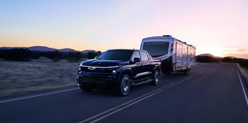 A 2025 Chevrolet Silverado EV towing a camper down the road.