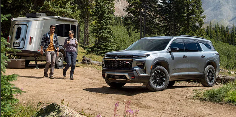 A man and woman walking from a camper toward a silver 2026 Chevrolet Traverse.
