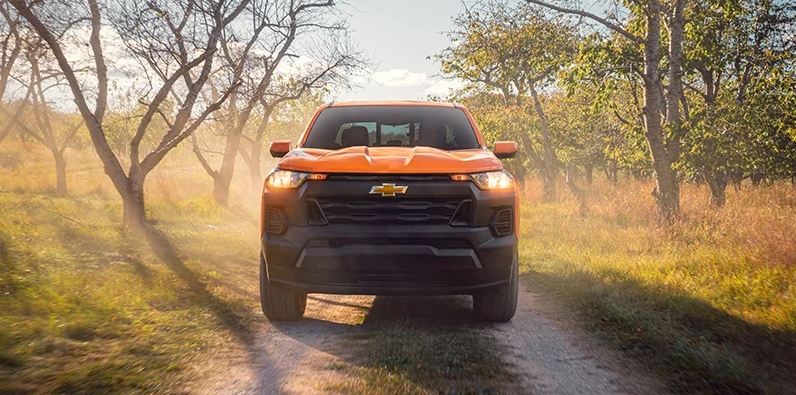 An Orange Chevy Colorado driving down a dirt road.