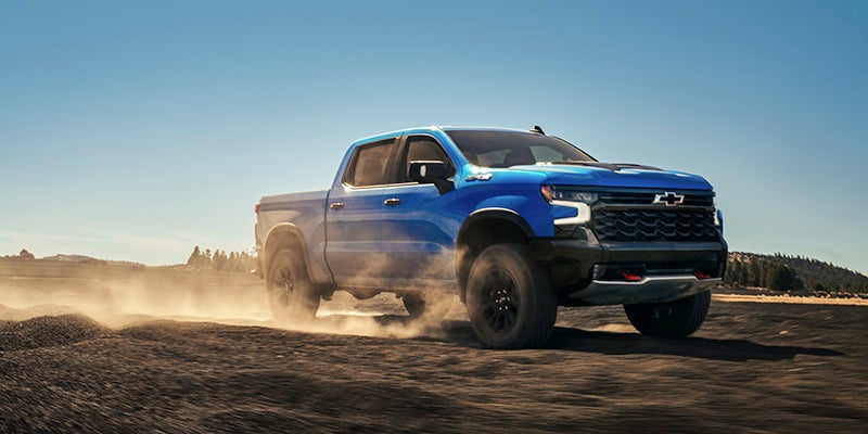 A blue 2025 Chevy Silverado 1500 truck driving through the desert.